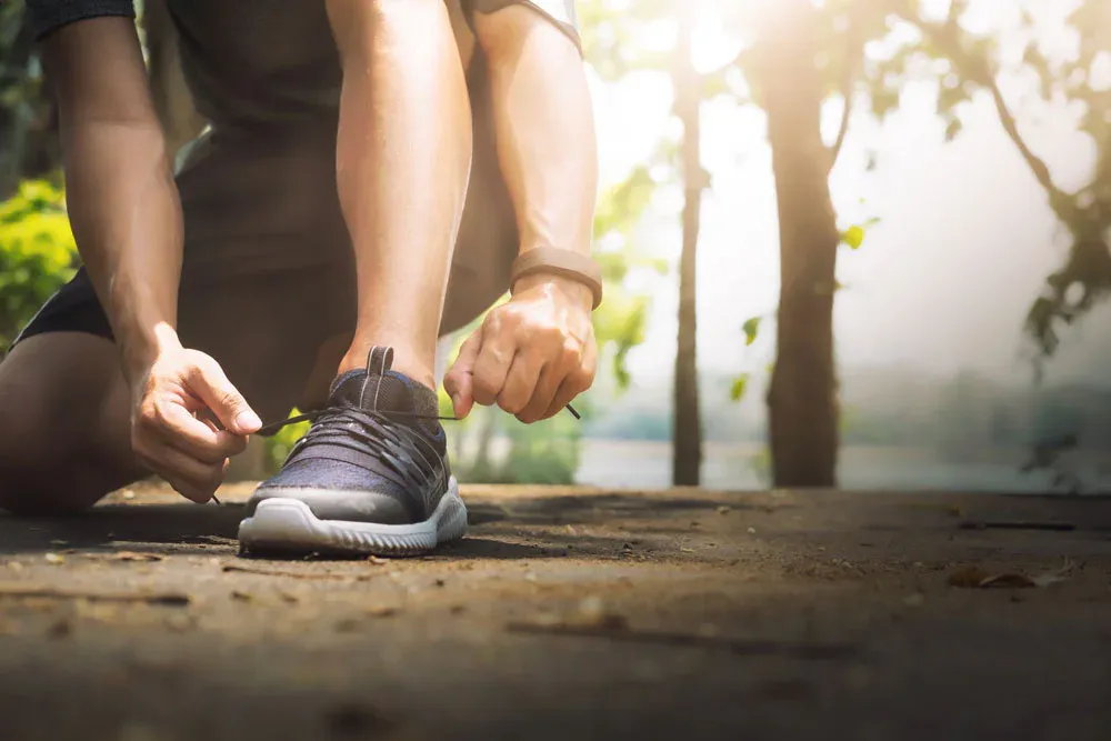 Runner kneeling to tie a running shoe on a forest path before a training session