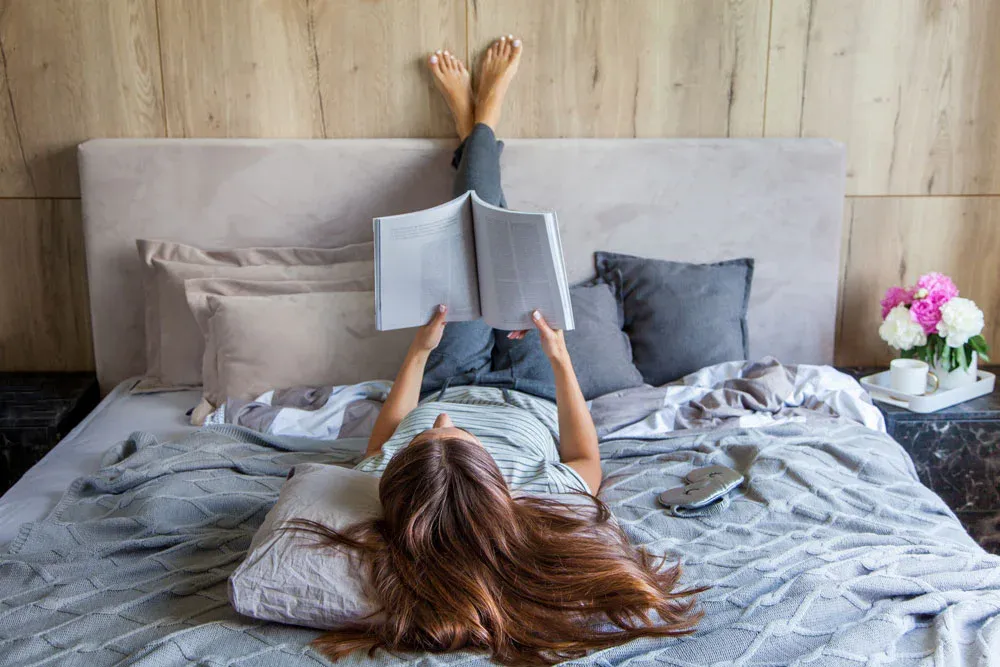 Woman relaxing on a bed reading a magazine, illustrating sleep and rest as part of training